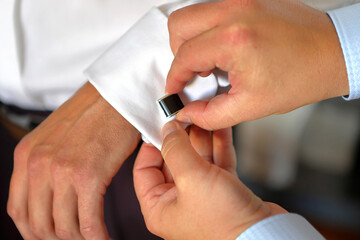 Best man puts a cufflink on the groom's cuff. Wedding preparations.