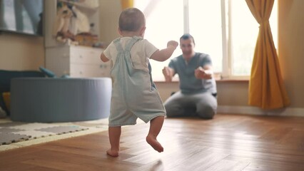 baby first steps. baby goes to her father at window learns to walk to take first steps. happy family kid dream concept. dad calls son baby first steps indoors lifestyle. happy family indoors concept