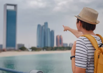 Foto op Canvas travel to the United Arab Emirates, Happy young asian female traveler with backpack and hat view to cityscape of downtown Abu Dhabi. Vacation and tourist destination concept. © YURII Seleznov