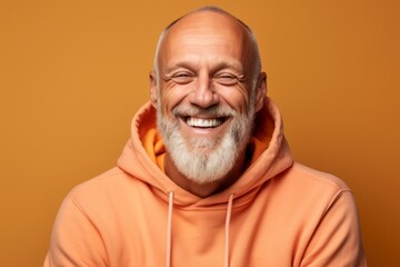 Headshot portrait photography of a joyful mature man wearing a comfortable hoodie against a pastel orange background. With generative AI technology