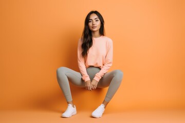 Lifestyle portrait photography of a glad girl in her 20s wearing a pair of leggings or tights against a pastel orange background. With generative AI technology