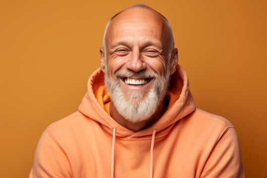 Headshot portrait photography of a joyful mature man wearing a comfortable hoodie against a pastel orange background. With generative AI technology