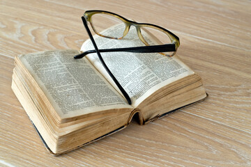 Old battered bible and glasses on a wooden table