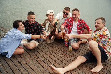 Celebrating, having fun. Group of friends are sitting near the lake with beer in hands