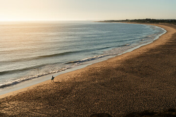 Paisaje de playa solitaria con figura de surfista andando por la playa solo con tabla de surf