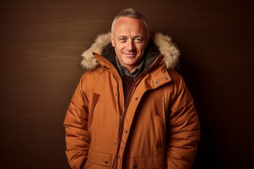 Lifestyle portrait photography of a glad mature man wearing a warm parka against a copper brown background. With generative AI technology