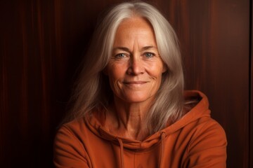 Fototapeta premium Photography in the style of pensive portraiture of a grinning mature woman wearing a comfortable hoodie against a copper brown background. With generative AI technology