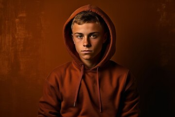 Medium shot portrait photography of a tender boy in his 20s wearing a cozy zip-up hoodie against a copper brown background. With generative AI technology