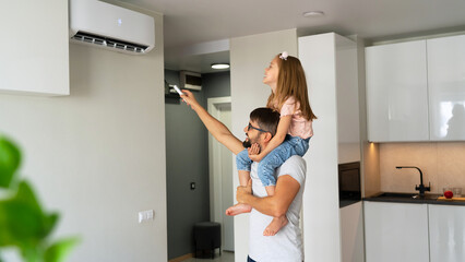 Happy family, father with little daughter on shoulders turn on air conditioner using remote control.