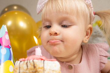 A two-year-old girl blows out a candle on a birthday cake, makes a wish