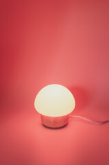 immagine con piccola lampada da tavolo a forma di fungo, base in legno, riflessi di luce, sfondo illuminato con luce rossa con ombre