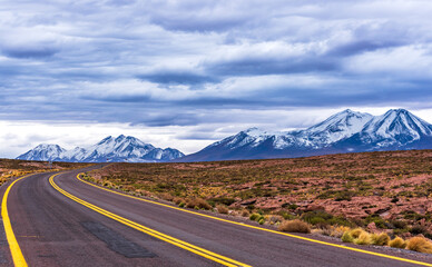 Curve in the infinitw road toward snowy mountains in Atacama desert