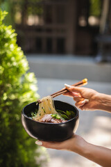 The girl's hands raise the noodles with bamboo sticks above the plate.