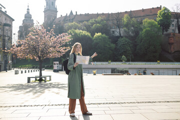 Traveller woman walking near famous old Wawel Royal Castle in Krakow holding tourist map shows the direction of the path. Travel and active lifestyle concept. Spring Cherry blossoms, pink flowers