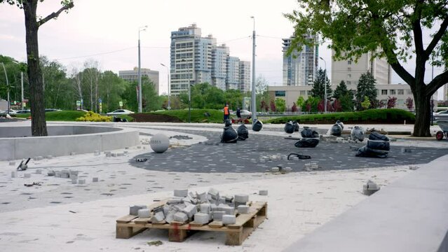 Construction debris lays around newly built park at daytime. Trash bags and stone bricks scattered about park in town center
