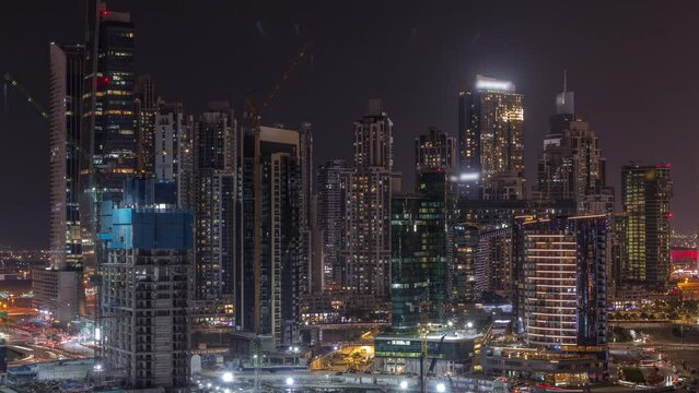 Cityscape with illuminated skyscrapers of Dubai Business Bay and water canal aerial night timelapse. Modern skyline with residential and office towers on waterfront. Buildings under construction