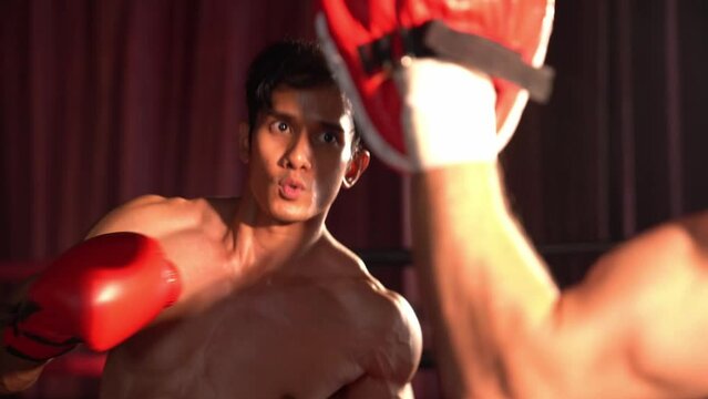 Asian and Caucasian Muay Thai boxer unleash punch in fierce boxing training session, delivering punching strike to sparring trainer, showcasing Muay Thai boxing technique and skill. Impetus
