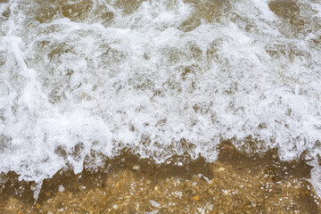 A sea foaming wave on the sandy seashore. Background of sea wave and coastal sand.  View from the top