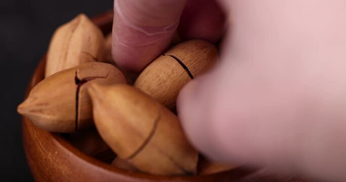 take a cracked unpeeled pecan close-up on the table, a pile of pecans in the shell