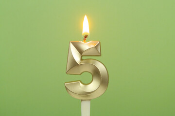 Gold birthday candle burning on green background. Number 5. Copy space for text.