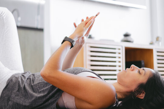 Latin woman lying on a yoga mat at home checking her mobile phone