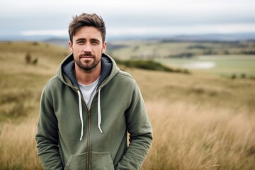 Environmental portrait photography of a glad boy in his 30s wearing a stylish hoodie against a rolling hills background. With generative AI technology