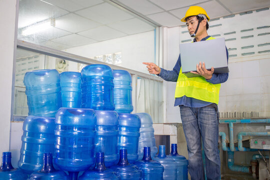 man worker and quality inspector using computer tablets check blue water gallons before shipment to contain drinking water.
