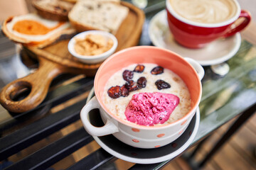Breakfast with fresh cooked porridge served with Dry Cherry with strawberry sorbet in bowl. Assorted sliced bread on a wooden board. Served with smoked butter. Breakfast with cappuccino coffee.