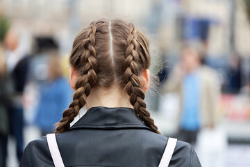 Girl with braided pigtails wearing leather jacket on a street. Female hairstyle and fashion in city