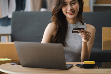 Asian woman holding credit card and using laptop. woman working at home. Online shopping, e-commerce, internet banking, spending money, working from home concept.