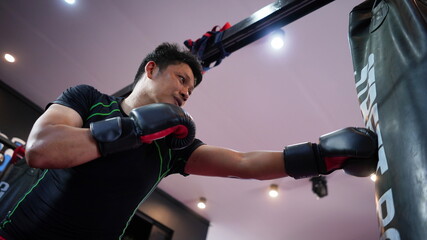 Thai boxing man in gym with sandbag. Athlete man in fitness with glove train in punching and...