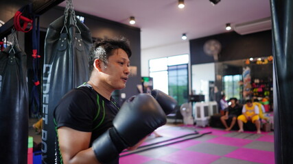 Thai boxing man in gym with sandbag. Athlete man in fitness with glove train in punching and...
