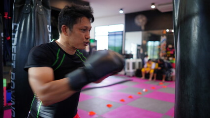 Thai boxing man in gym with sandbag. Athlete man in fitness with glove train in punching and...