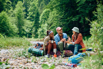 Happy backpackers using cell phone while relaxing during their hiking day in woods.