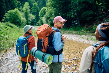 Fototapeta na wymiar Happy hiker talks to his friends while walking with backpacks through woods.