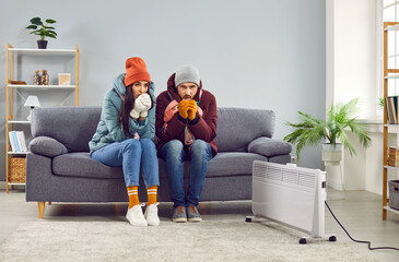 Full length photo of a young frozen family couple man and woman sitting on sofa in the living room...