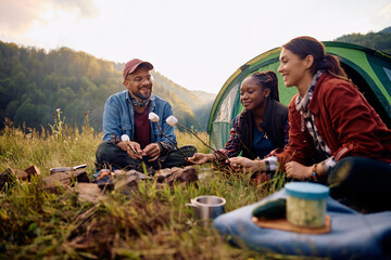 Happy friends roasting marshmallows while camping in nature.
