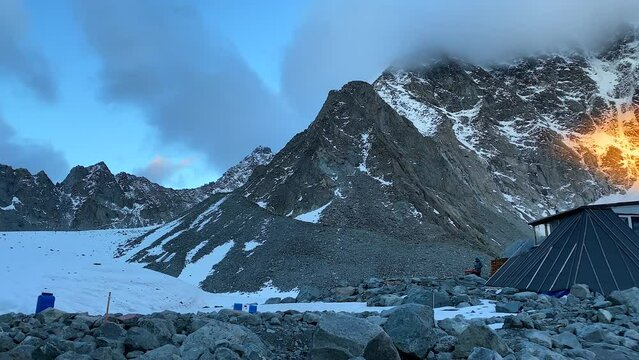 Beautiful golden sunset in the mountains. A house for climbers. Climbing Belukha. Amazing panorama of snow-covered hills, rocks, ridges and slopes of the Altai mountains. Calm natural background.