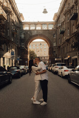 The couple walks around Kyiv. Old city. Love story. Walk around the city. A woman in a white suit. Guy in a t-shirt and jeans. Love and hugs. To cross the road. No focus blurred and noise effect