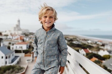 Lifestyle portrait photography of a grinning kid male wearing a chic jumpsuit against a scenic coastal village background. With generative AI technology