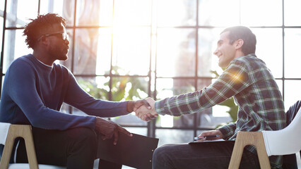Business partners shaking hands sit on chairs in office lobby start or finish successful negotiations.