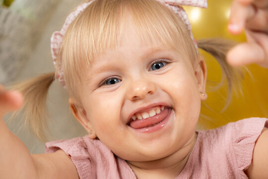 Two-year-old girl smiling looking at the camera, sticking out her tongue, drooling in children, teething.