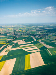 Aerial view with the landscape geometry texture of a lot of agriculture fields with different plants like rapeseed in blooming season and green wheat. Farming and agriculture industry.