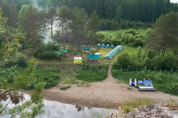 Rafters' tent camp on the river bank. Tents stand in a green clearing against the background of the forest.