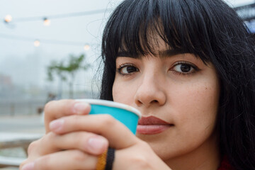 closeup of young latin woman watching the camera outdoors with a hot drink