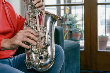 close up in profile with copy space of male hands playing a saxophone inside home.