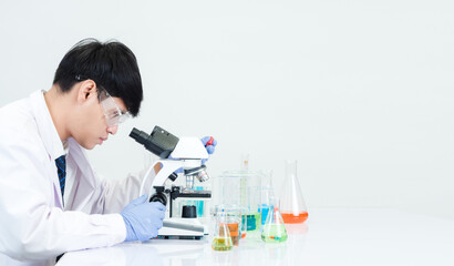 Fototapeta premium Asian man student scien Wearing a doctor's gown in the lab looking hand at chemist. caused by mixing reagents in scientific research laboratories with test tubes and microscope on the table