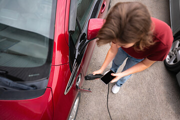 Woman with smartphone charging red electric car.