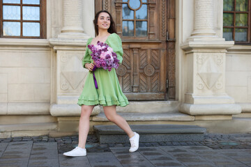 Beautiful woman with bouquet of spring flowers near building outdoors