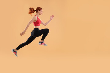 Fototapeta na wymiar Young woman in sportswear jumping on beige background, space for text